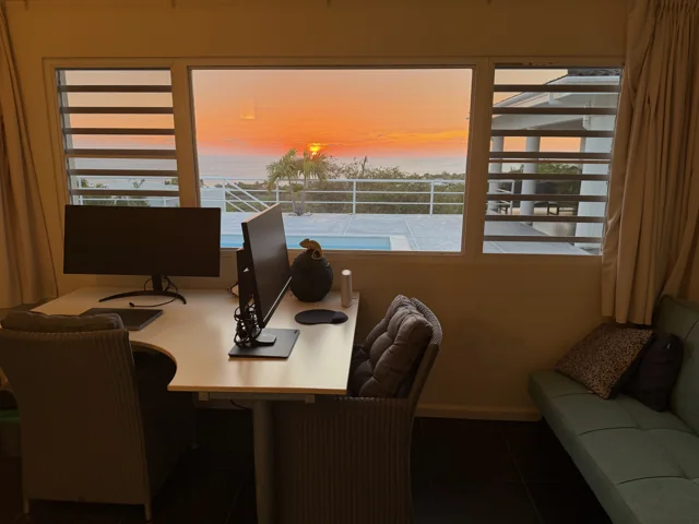 Kantoor met twee monitoren en slaapbank, met zonsondergang boven zee